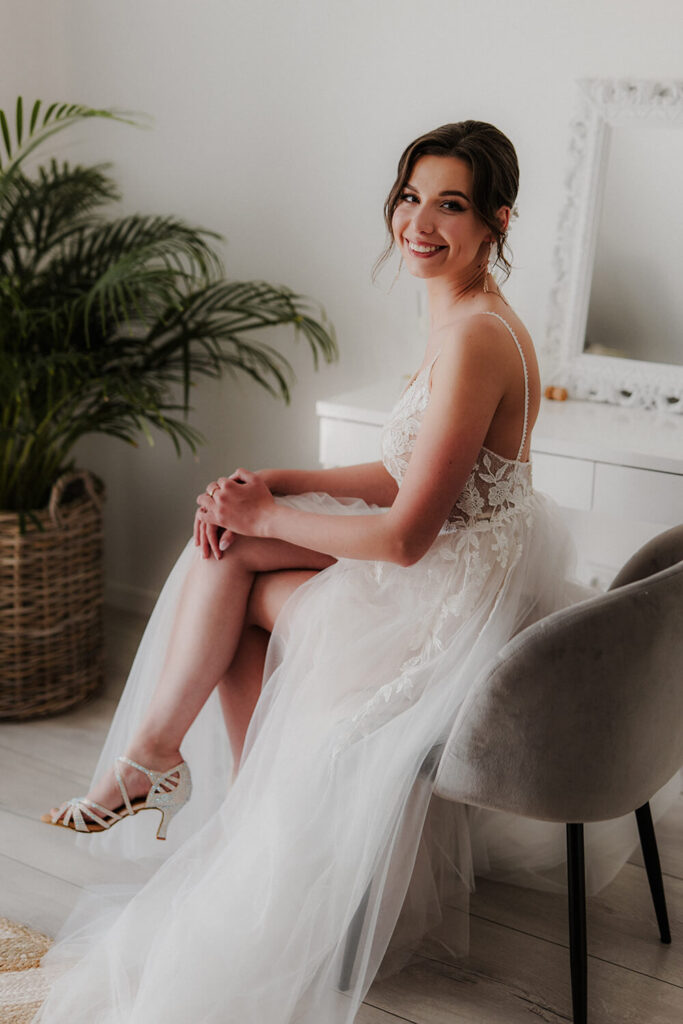 Panna młoda siedzi przy lustrze, zwrócona w stronę aparatu i się uśmiecha