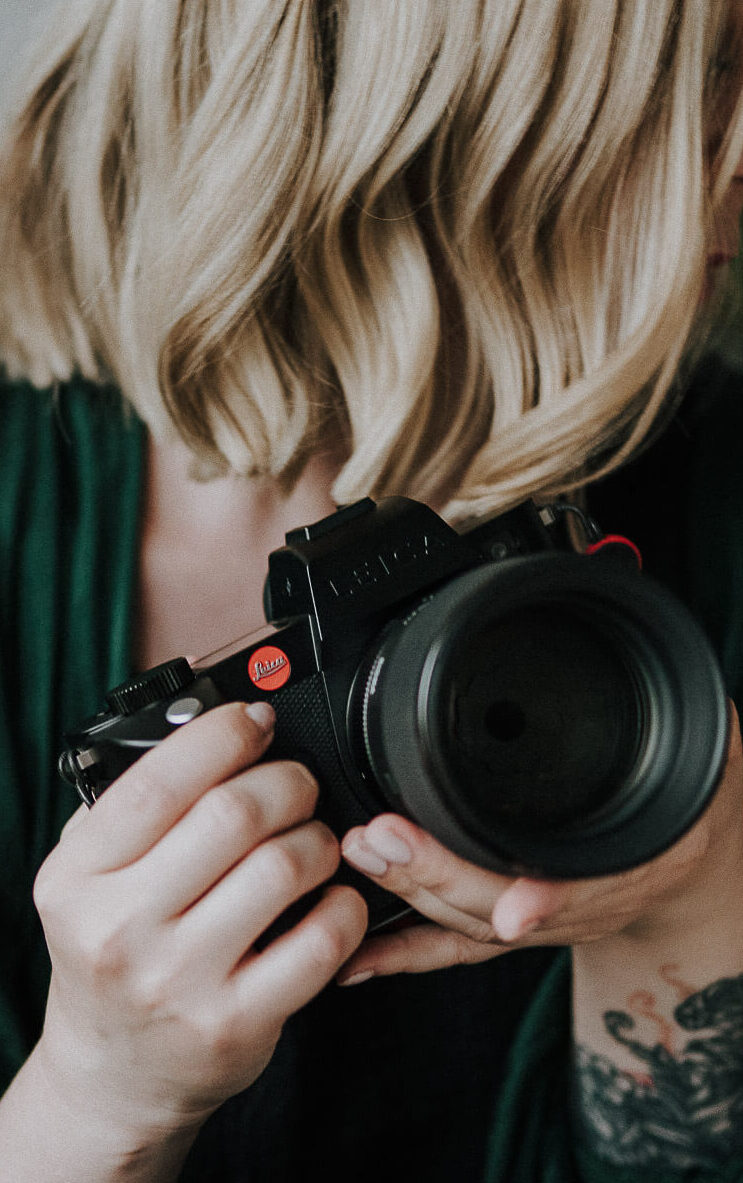 Fotografka trzyma w ręku aparat Leica, Którym wykonuje naturalne reportaże ślubne i sesje zdjęciowe