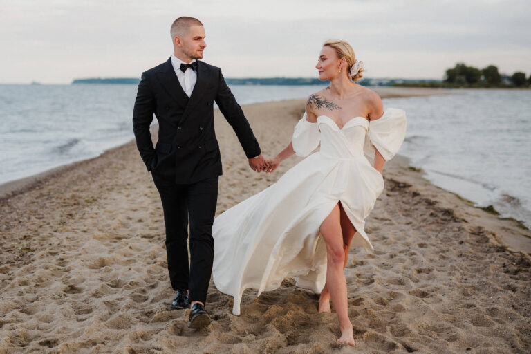 Para młoda spaceruje plażą w czasie sesji ślubnej nad morzem wykonanej na Cyplu Rewskim