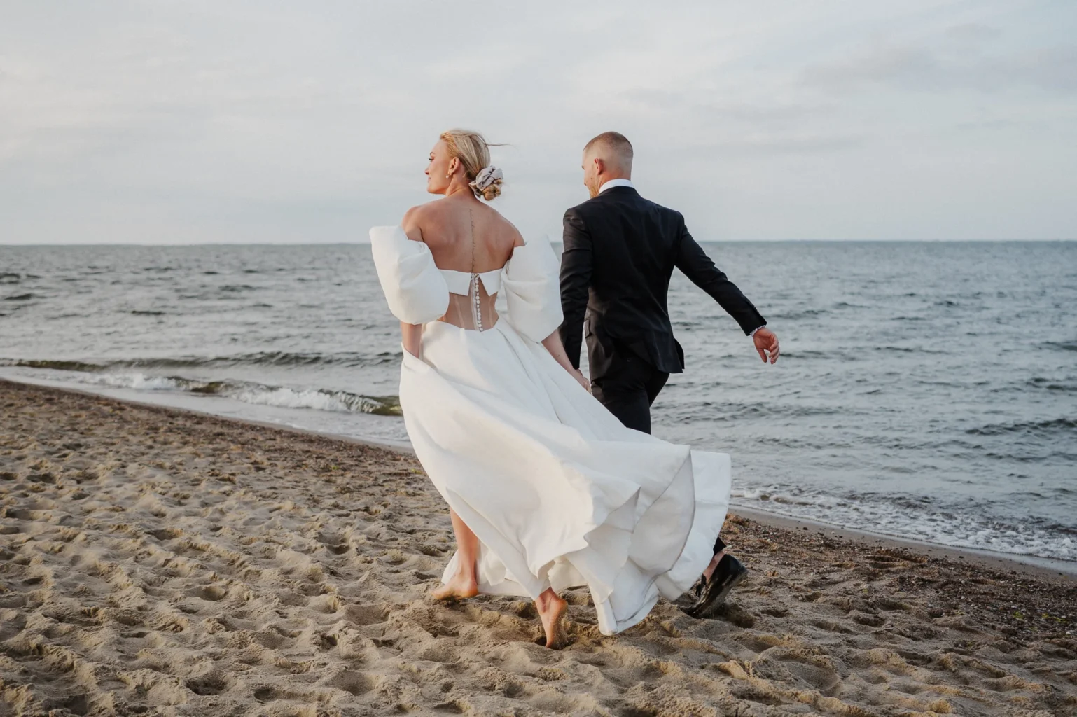 Para młoda biegnie wzdłuż plaży w czasie sesji zdjęciowej w Rewie