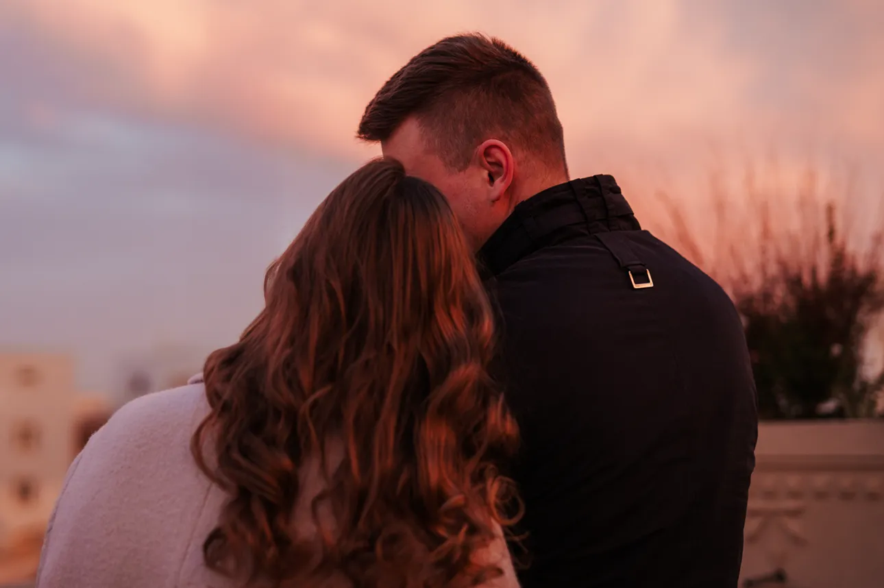 Para zakochanych stoi przytulona, oświetlona różowym światłem wschodzącego słońca