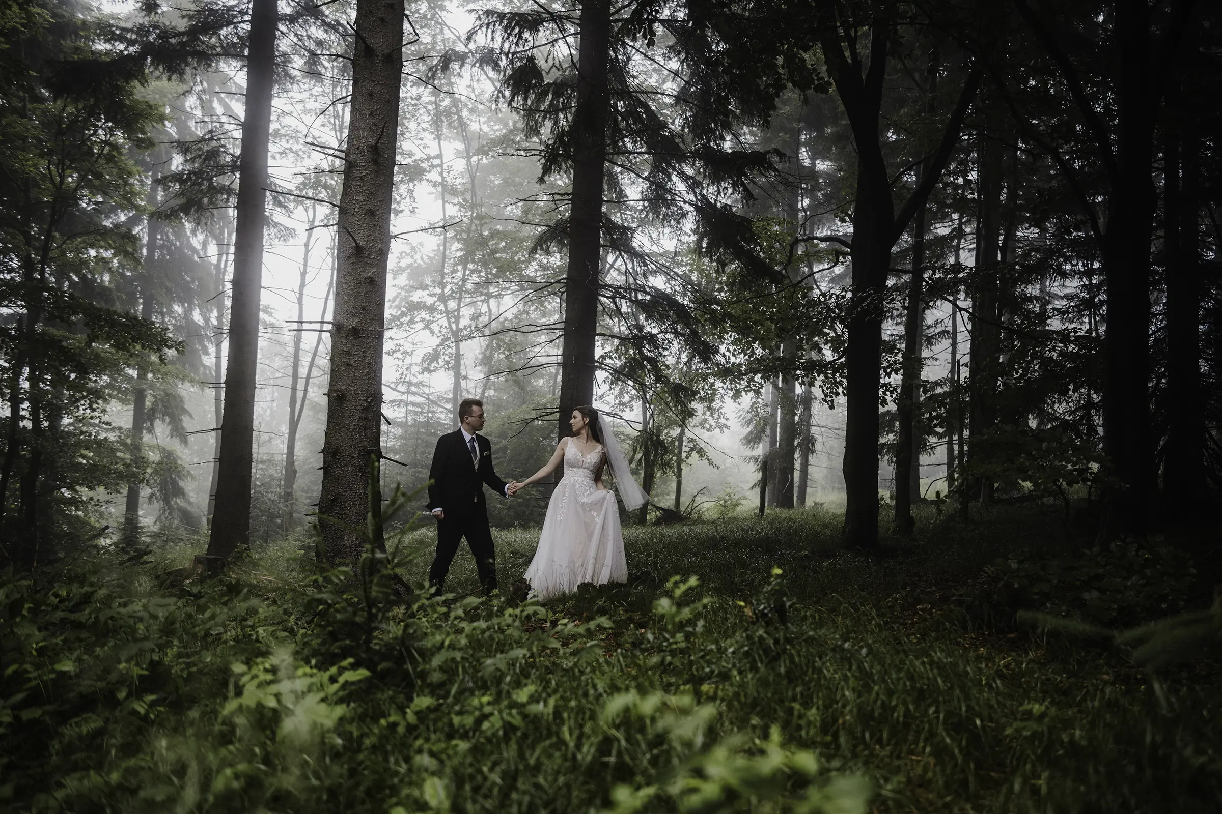Para młoda spaceruje w zamglonym lesie w czasie naturalnej sesji ślubnej wykonanej w okolicach Wrocławia