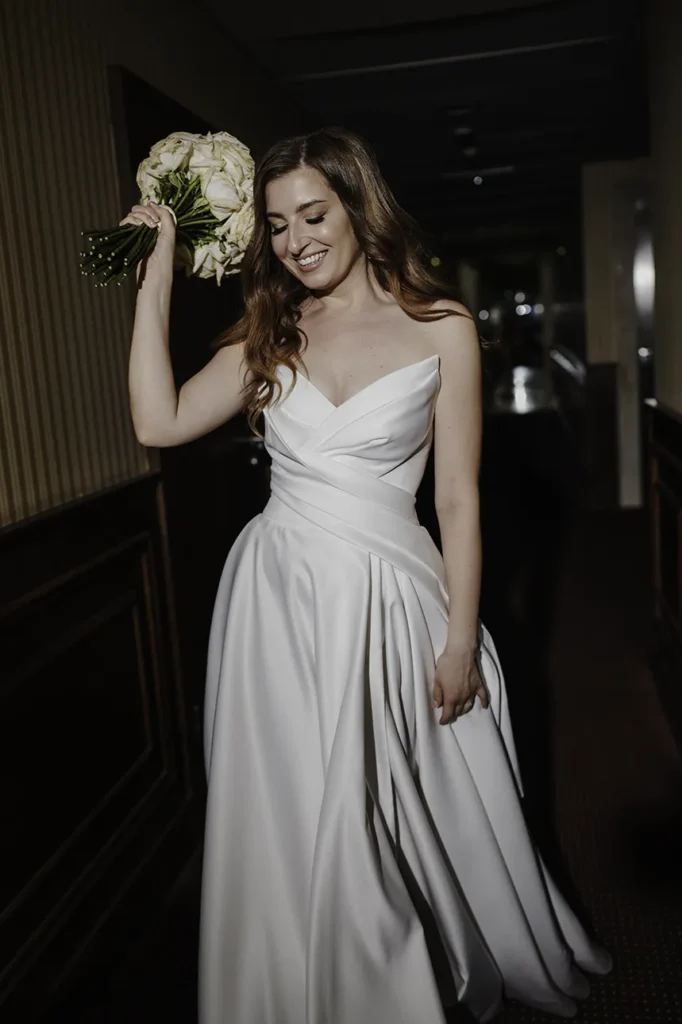 Panna młoda idzie hotelowym korytarzem, trzymając w dłoni bukiet