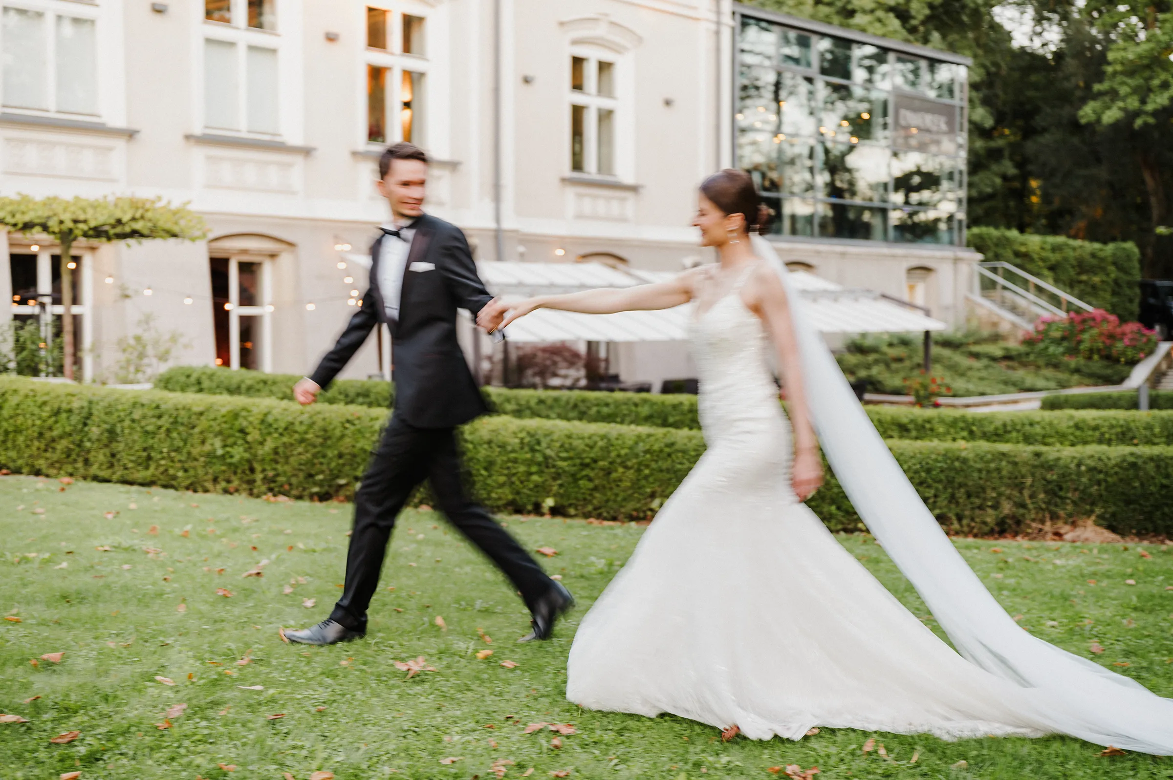 Para młoda patrzy na siebie, trzymając się za ręce i spacerując na tle dworku.