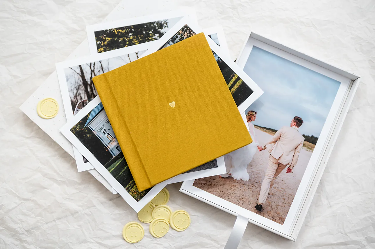 Fotoalbum leżący na stosie odbitek i wydruków zdjęć, które możecie zamówić w ramach mojej oferty fotografii ślubnej